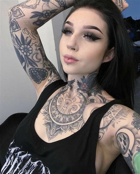 a woman with lots of tattoos on her chest posing for the camera while