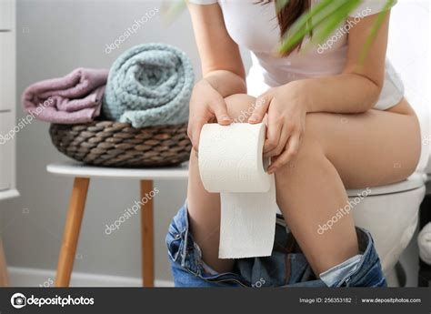 Young Woman With Soft Paper Sitting On Toilet Bowl In Restroom Stock