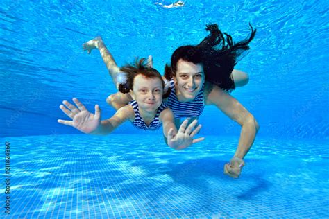 Happy Mom And Daughter Swim Underwater In The Pool In Striped Swimsuits