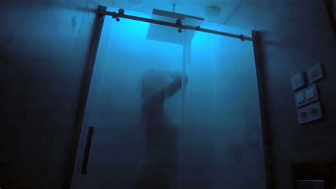 naked woman taking a shower behind glass screen in a
