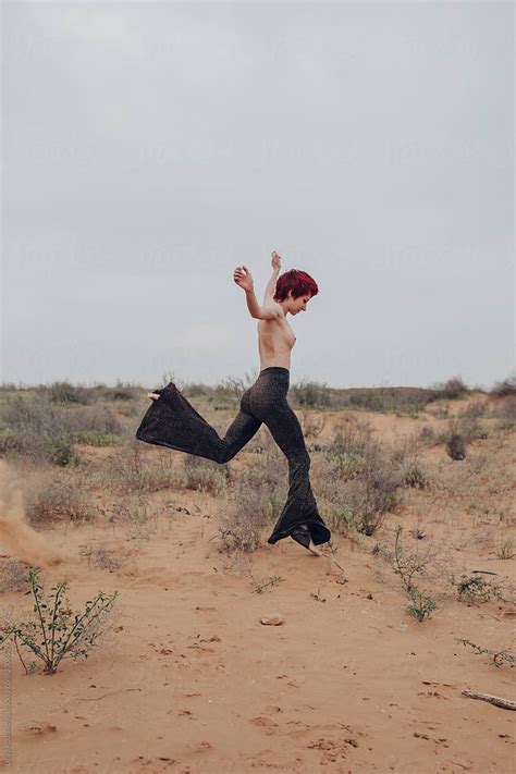 redhead topless female in disco styled pants jumping in desert by