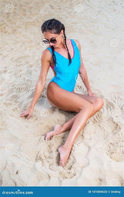 vrouwelijk model met slank lichaam die zwempakzitting alleen op zandig strand dragen stock