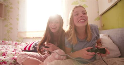 teen girl on a bed pushing her laughing friend in a joking way while playing computer games at a