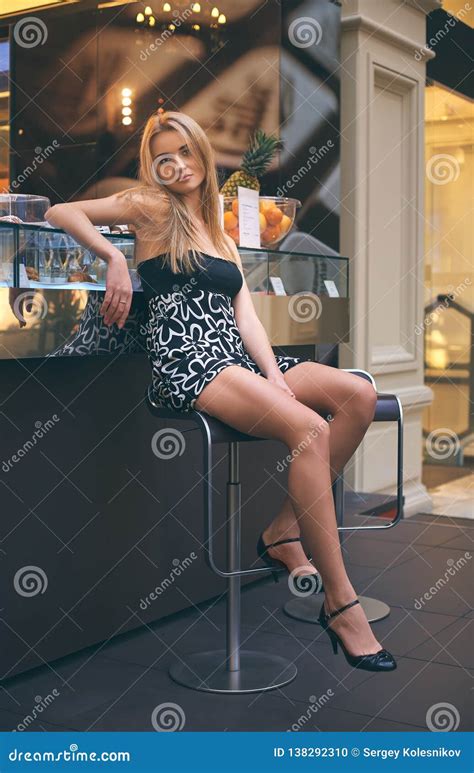 Attractive Blonde Girl With Long Hair Sitting On A High Bar Stool Stock