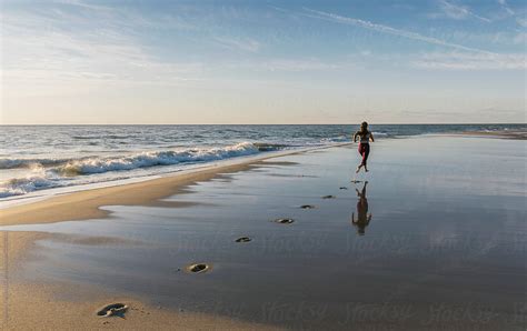Fit Female Athlete Making Footprints While Running On Beach By