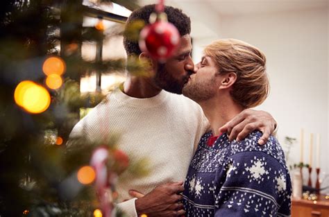 Gay Male Couple Kissing As They Hang Decorations On Christmas Tree At