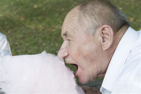 An Elderly Man In A White Shirt With His Mouth Wide Open Bites Off A