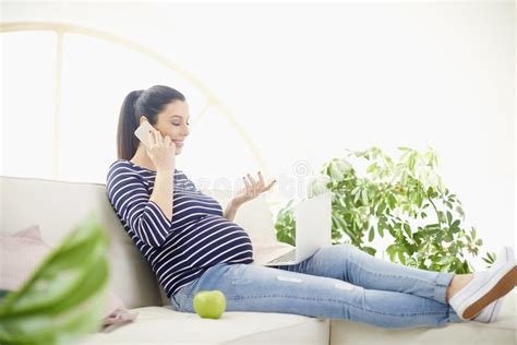 pregnant woman talking on her mobile phone and using notebook stock