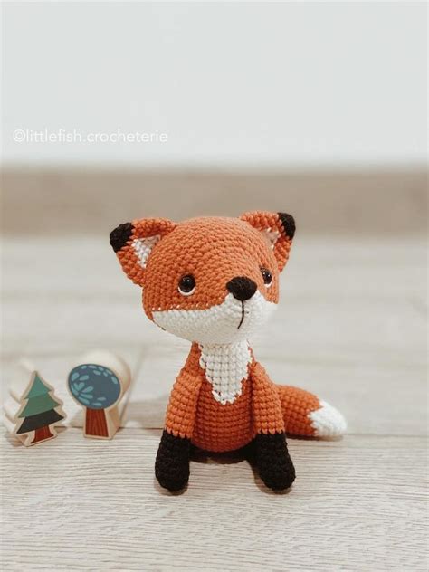 An Orange Knitted Fox Sitting On Top Of A Wooden Floor Next To A Pin