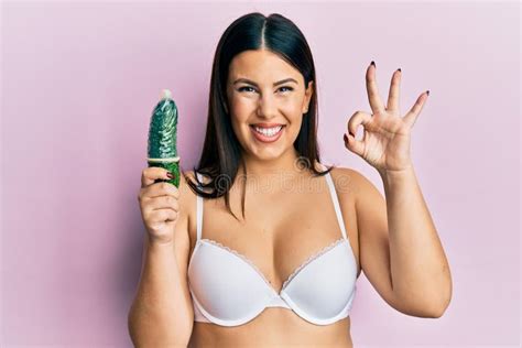 beautiful brunette woman holding condom on cucumber for sex education
