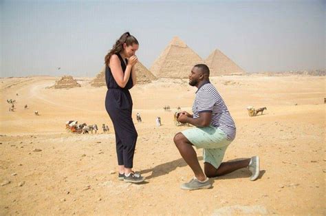 A Man Kneeling Down Next To A Woman In Front Of The Pyramids