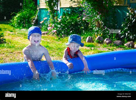 Brother And Sister Playfully Splashing Around The Blue Inflatable Pool