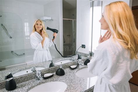 Attractive Mature Woman In Bathrobe Drying Hair With Hair Dryer In