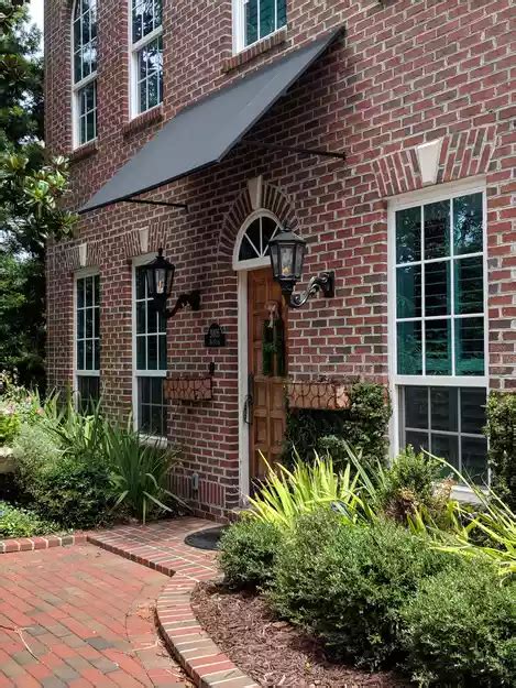 red brick house  green shutters  white trim   front door  surrounded  greenery