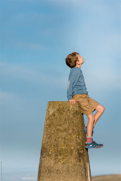 child sitting  trig point pillar     sky  stocksy
