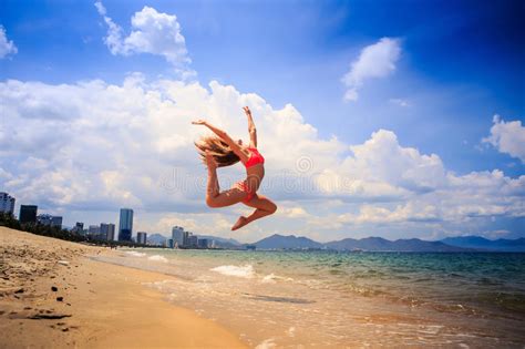 Blonde Slim Gymnast In Bikini In Jump Over Beach Against