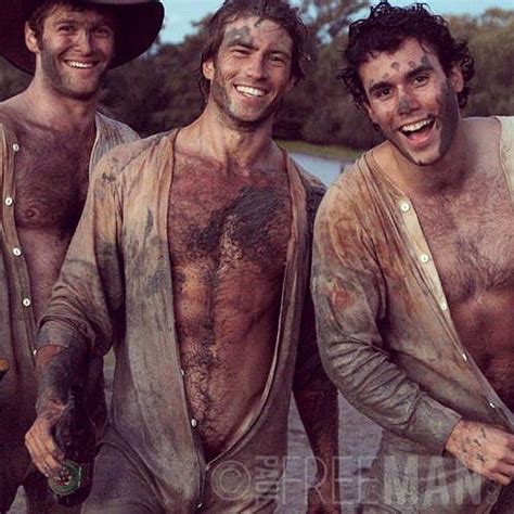 three men with mud on their bodies and one holding a bottle in his hand