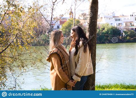 lesbian couple leaning against a tree in a park with their hands