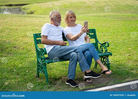 Elderly Couple Sitting Together On Bench In Public Park And Video Call