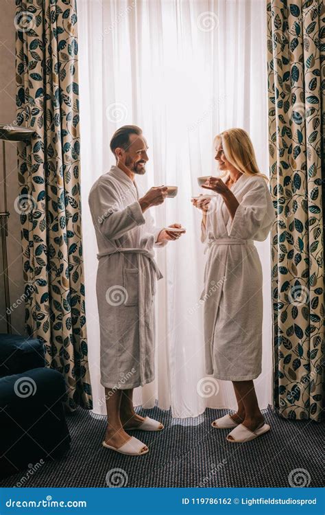 Side View Of Happy Mature Couple In Bathrobes Drinking Coffee And