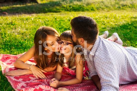 Happy Mother Father And Kissing Their Daughter In The Park Stock
