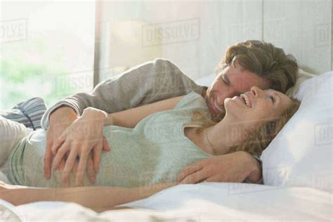 Affectionate Pregnant Couple Laying In Bed Laughing
