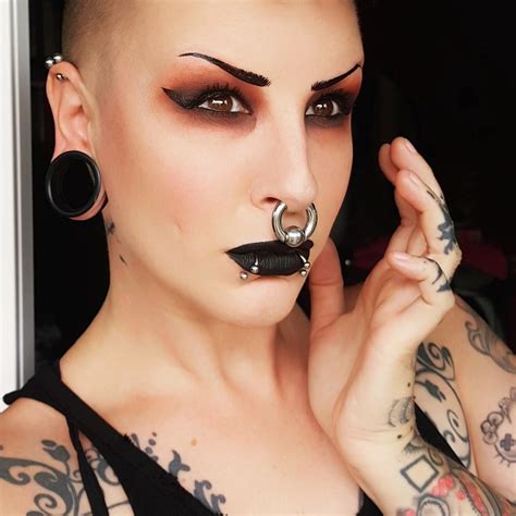 A Woman With Black Makeup And Piercings Holding Her Nose To The Side
