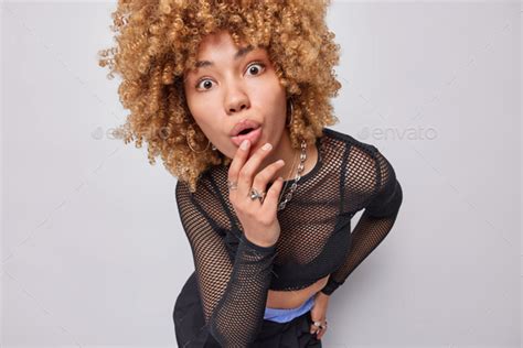 photo of surprised curly haired woman keeps mouth widely opened stares