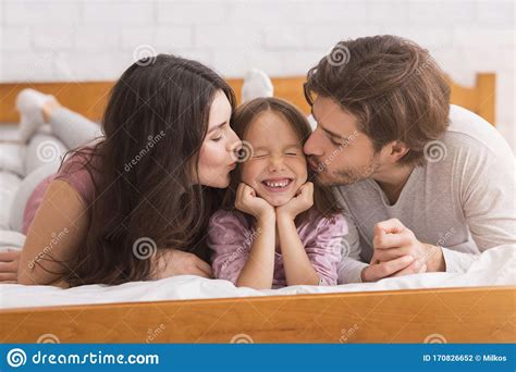 Loving Mother And Father Kissing Their Little Daughter In Bed Stock