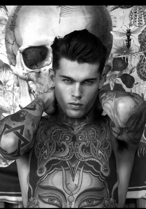 A Man With Tattoos On His Chest And Hands In Front Of Two Human Skull Heads