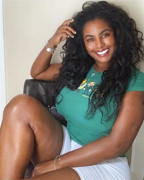 A Woman Sitting On Top Of A Chair Wearing A Green Shirt And White Skirt
