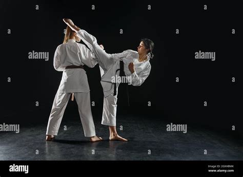 Two Female Karatekas In White Kimono Strike In Action Dark Background