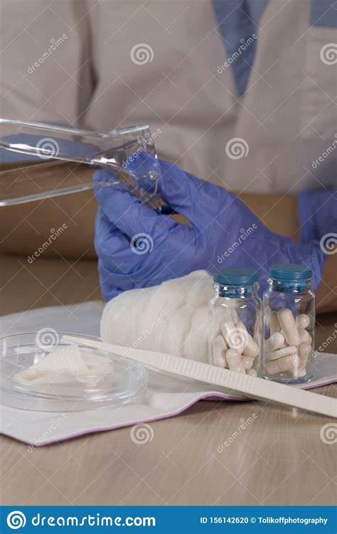glass bottles with pills in front of gynecologist who keeps vaginal speculum closeup stock
