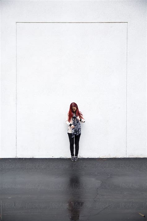 woman with red hair standing in front of a large wall by stocksy