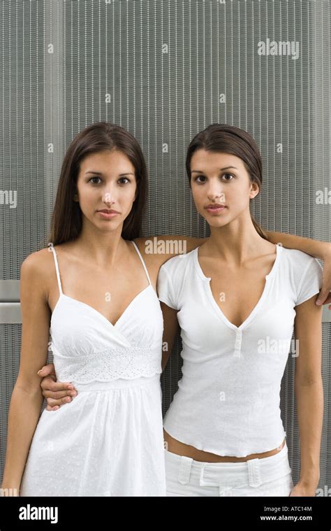 Twin Sisters Standing With Arms Around Each Other Looking At Camera