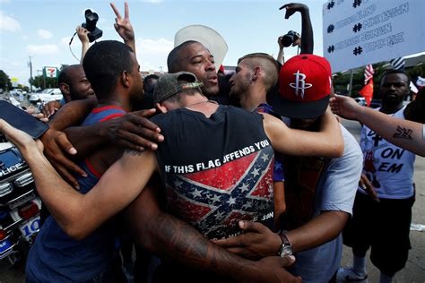 people including a man wearing a confederate flag hug after taking part in a prayer circle
