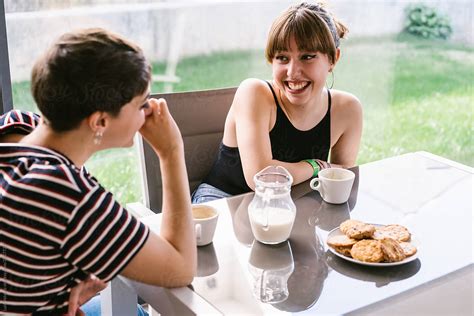 two girls talking and smiling while having a coffee at home by