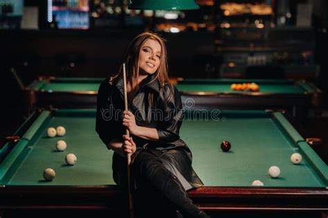 a girl with a cue in her hands sits on a table in a billiard club