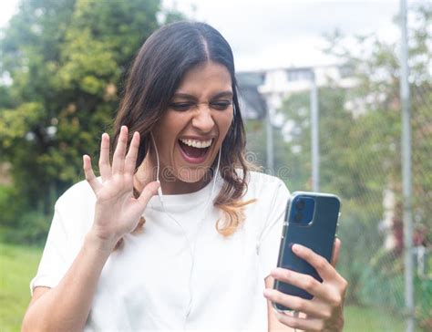 Smiling Latina Woman Waving At Cell Phone Camera In Video Call Stock