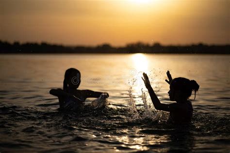 Two Sisters Splashing Water Playing In The Lake At Sunset Background