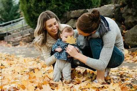 two lesbian moms looking at fall leaves with infant daughter outside