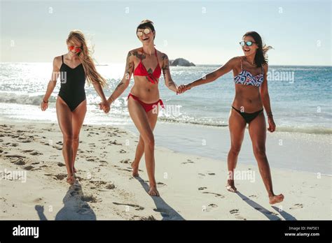 Three Girlfriends In Bikini Wearing Sunglasses Walking On Beach Holding