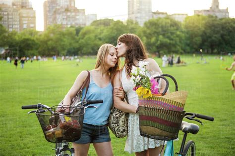 Romantic Lesbian Couple Standing With Bicycles On Grassy