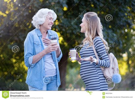 Joyful Pregnant Woman Enjoying Conversation With Aged Mother Outdoors