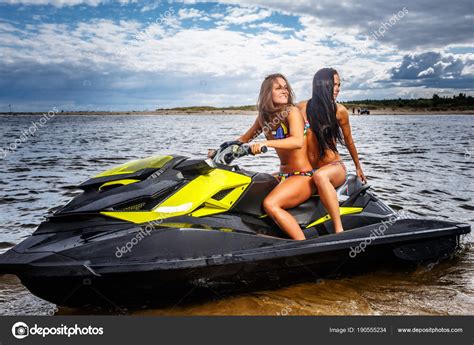 Two Sexy Girls In A Swimwear Sitting On A Jet Ski Have Fun At A