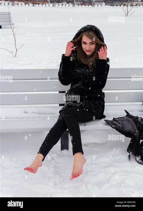 a beautiful russian woman with bare feet sits on a bench in the winter