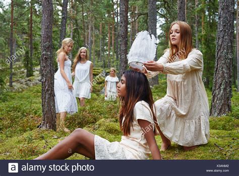 teenage girl putting white hat on friend in forest stock