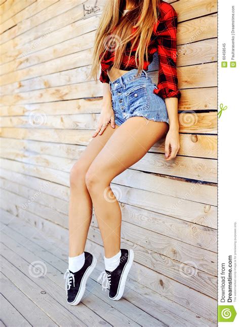 Hot Tan Slim Woman Legs In Sneakers And Jeans Shorts