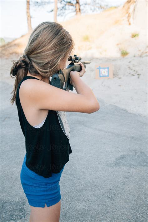 teen girl shooting a pellet gun at a target in the sand by carolyn