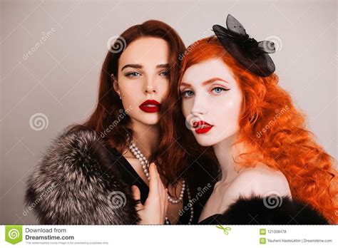 dos muchachas lesbianas fabulosas jovenes con el pelo largo rizado en vestido negro en fondo